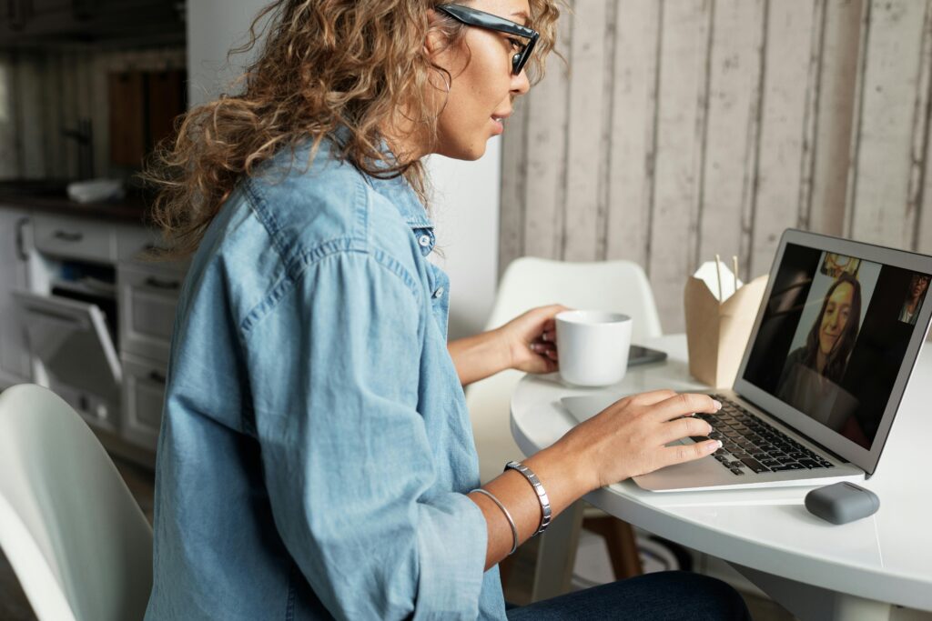 A woman attends a virtual therapy session from home on her laptop, drinking coffee during her Arizona Virtual IOP meeting.
