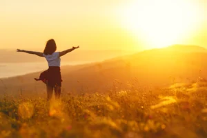 Person standing in a sunlit field at sunrise with arms open, symbolizing hope and healing.