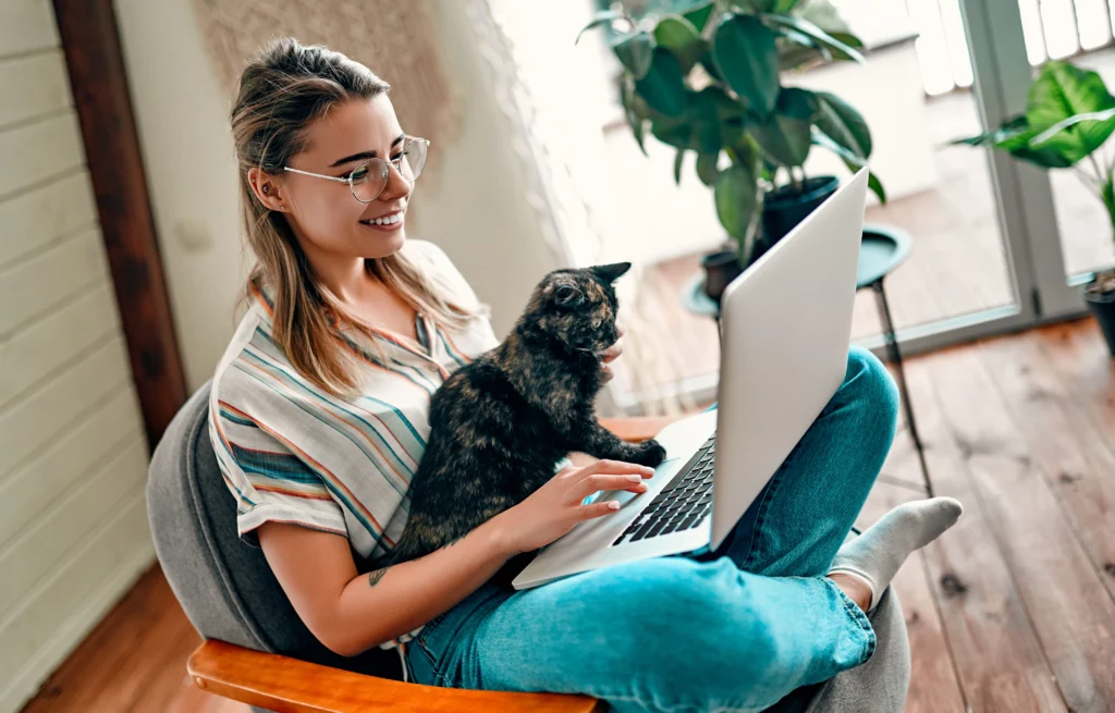 woman sits with her cat on the couch while holding her laptop while she does online therapy
